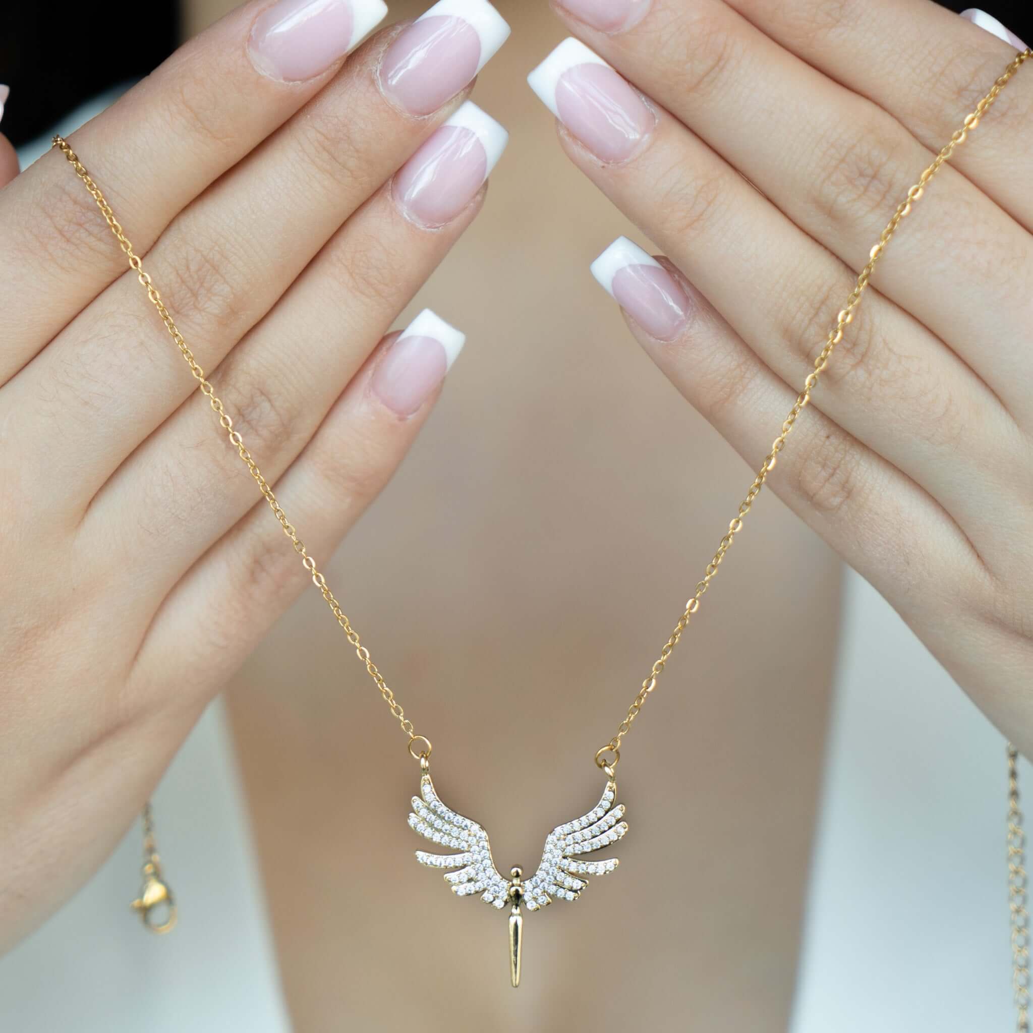 Engelsflügel Halskette in Gold mit funkelnden Kristallen, getragen von einer Person mit gepflegten Nägeln.