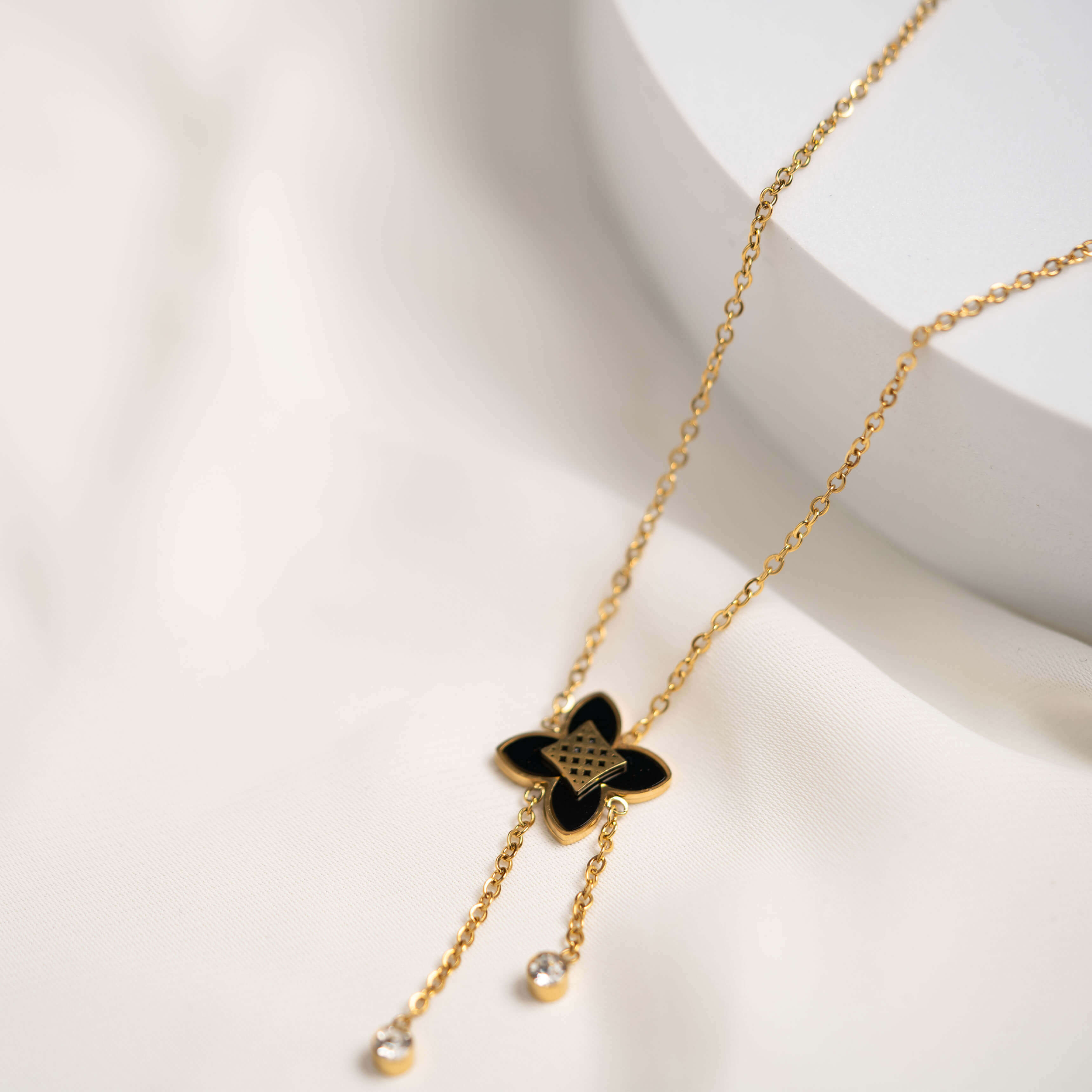 Goldene Kleeblattkette mit Kristallanhängern auf weichem Stoffhintergrund, elegantes Design und filigranes Look.